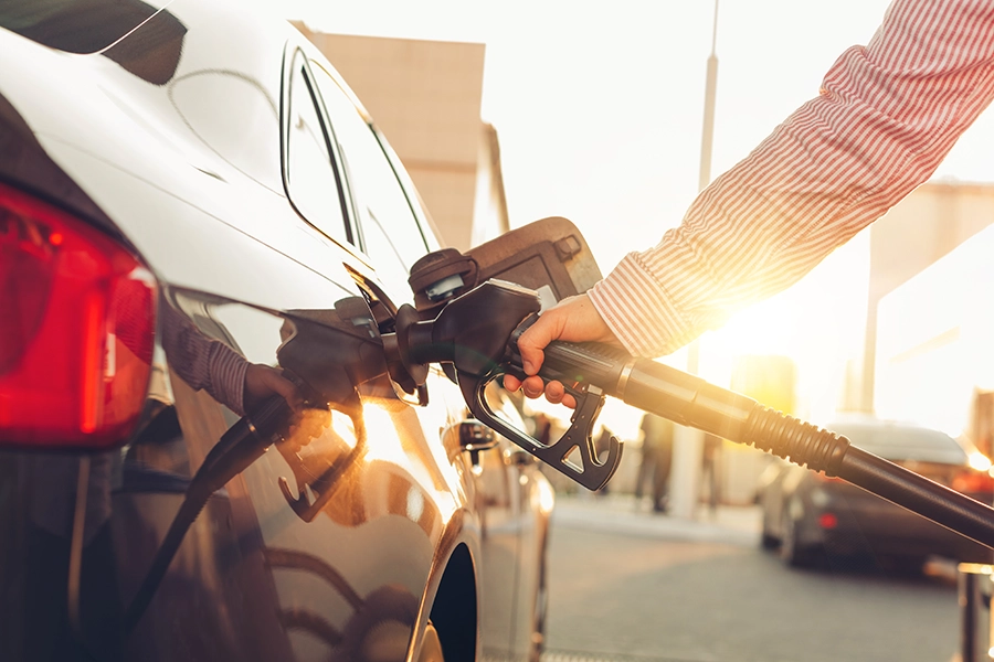 Person refueling white car at gas station with fuel pump nozzle inserted in tank
