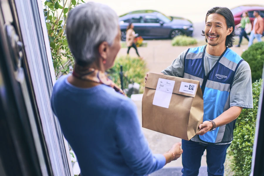 Amazon delivery partner in a blue vest handing a package to customer at their front door