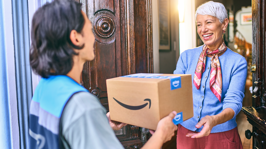 Man in a blue vest handing an Amazon package to a customer at her doorstep