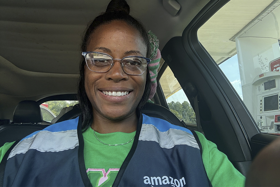 Woman in a blue vest smiling in the driver's seat of a car