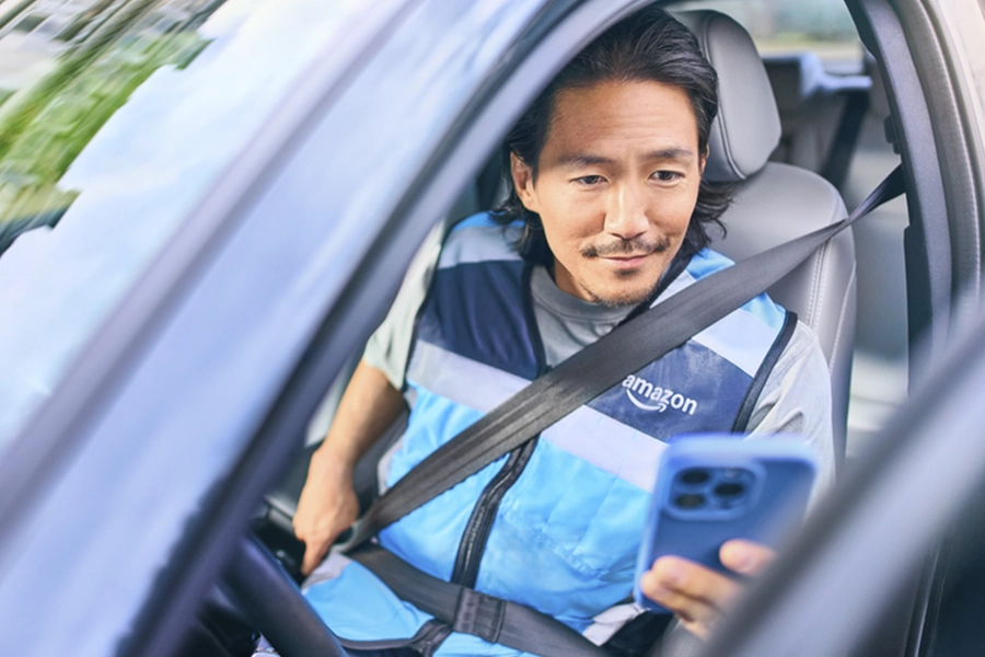 Man in a blue Amazon vest looking at his phone while stepping out of his vehicle