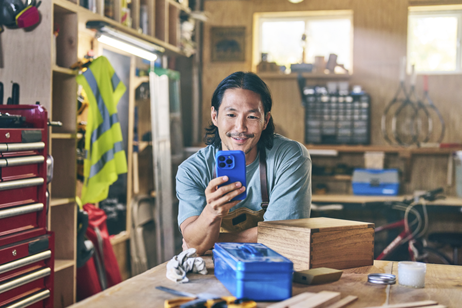 Man in a workshop leaning on a table looking at his phone